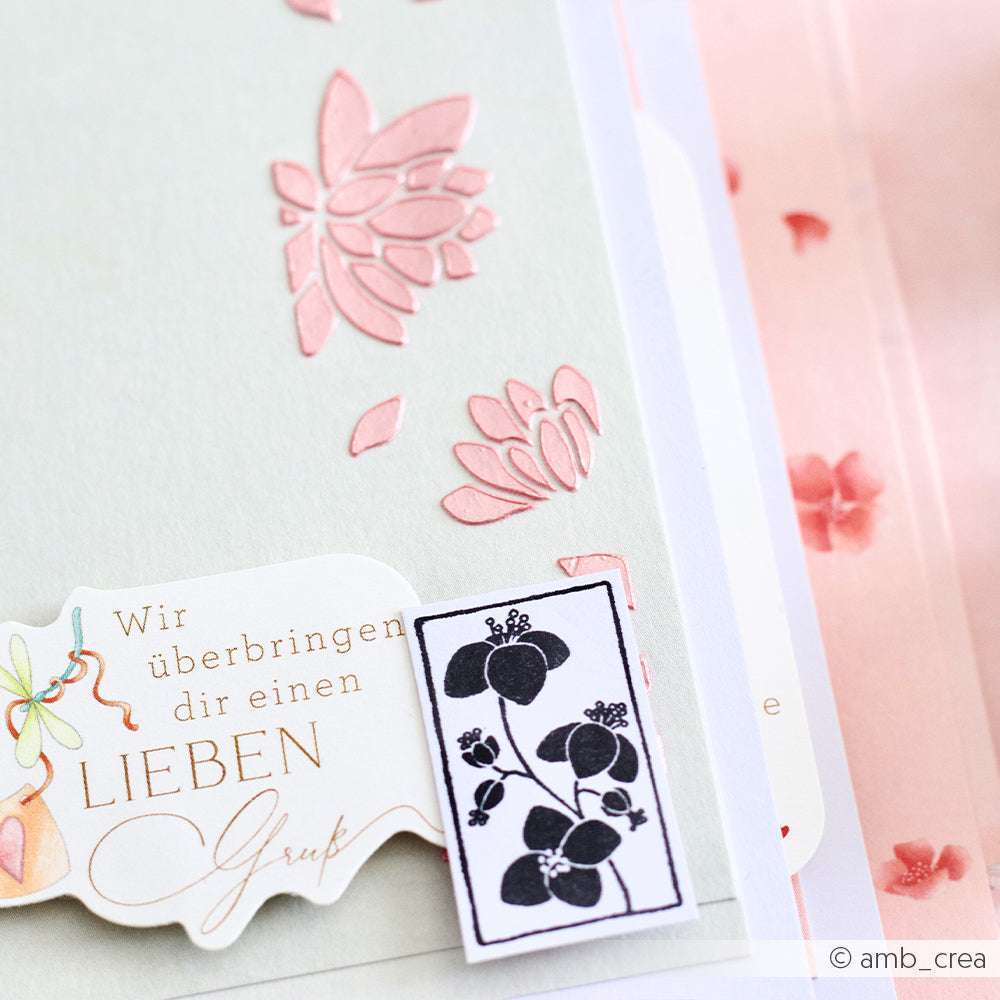 Eine Nahaufnahme der pastellfarbenen Grußkarten von Alexandra Renke mit geprägten Blumen, deutschem Text, einem schwarzen Blumenaufkleber, zarten Blütenornament-Akzenten und subtilen, von Stempelgummi inspirierten Basteldetails.