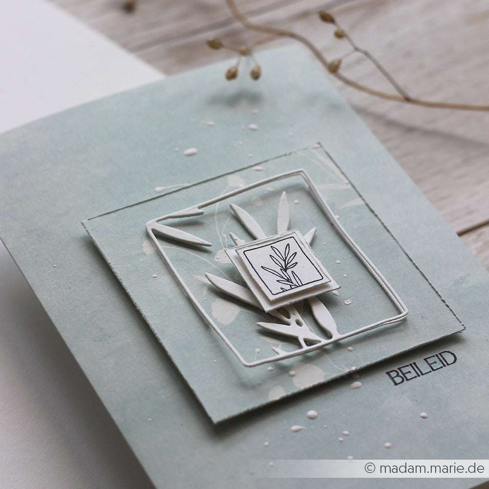 Minimalistische Kondolenzkarte von Alexandra Renke mit einem handgezeichneten Blatt, Gräserornament Outline, geschichteten weißen Papierblättern und dem Text "BEILEID" auf hellblauem Grund.