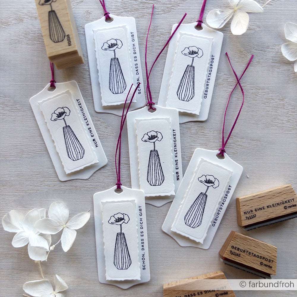 Sieben weiße Geschenkanhänger von Alexandra Renke, jeder mit einer Blumenvase Stempel-Illustration und deutschem Text, mit lila Schnur gebunden und auf einer hellen Fläche ausgestellt.
