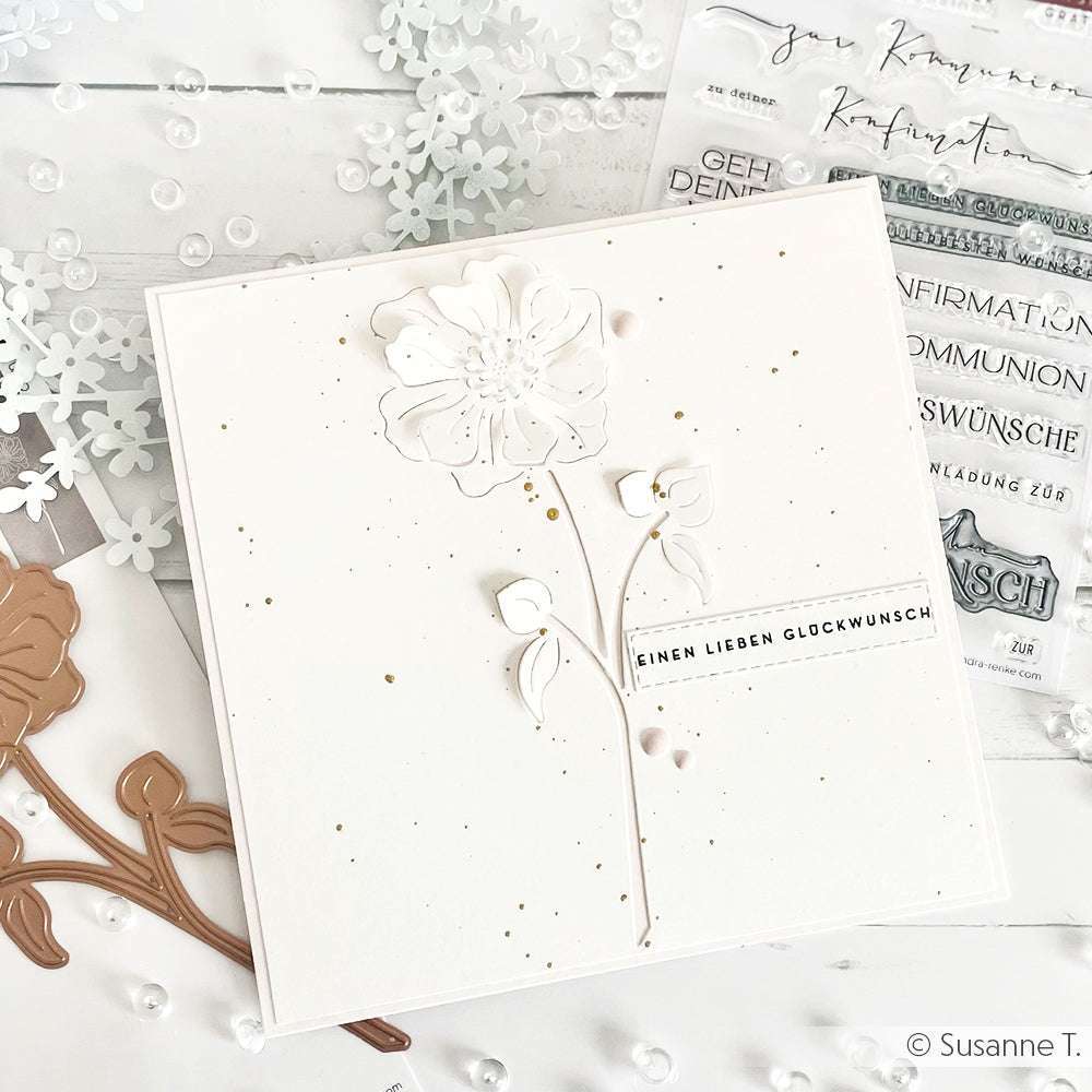 Handgefertigte weiße Karte von Alexandra Renke, mit einer geprägten Blume mit der Motivstanze Negativ-Blume 4, Goldspritzern, hochwertigem Designpapier und einem deutschen Grußstreifen auf der Vorderseite.