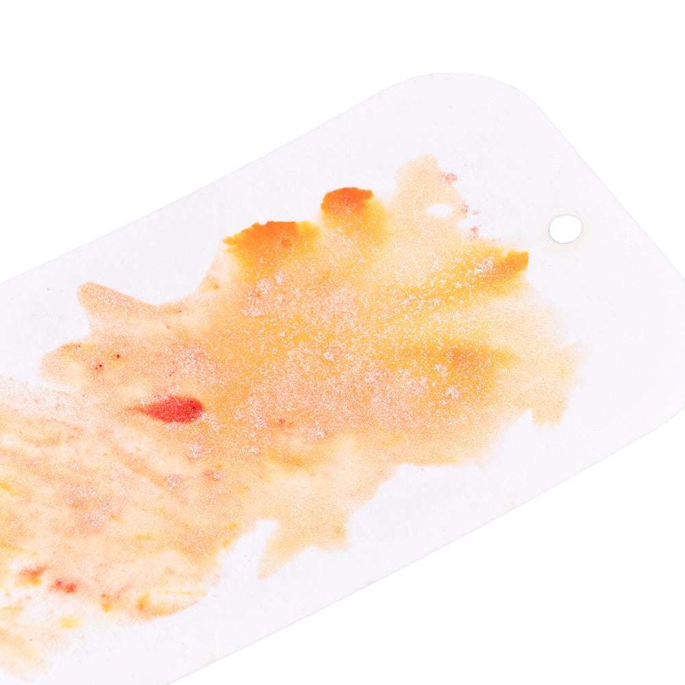 Weiße Karte mit einem orangefarbenen und gelben Aquarellspritzer, roten Tupfen, die mit Lindy's Stamp Gang hochpigmentiertem Pulver hergestellt wurden, und einem kleinen runden Loch auf der rechten Seite.