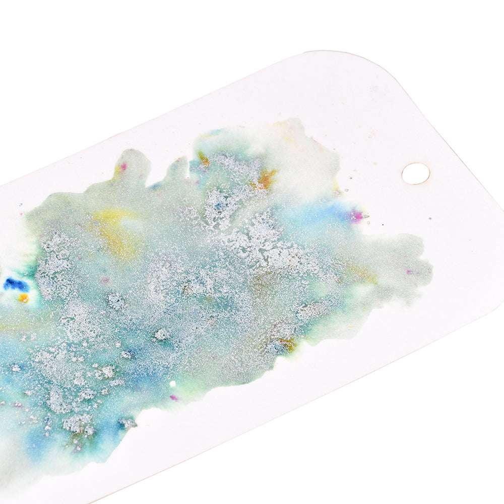 Abstraktes Kunstwerk in blauen und grünen Aquarellfarben, erstellt mit Lindy's Stamp Gang vibrant Pigmente auf einem weißen Papieranhänger, mit einem Loch in der Ecke.