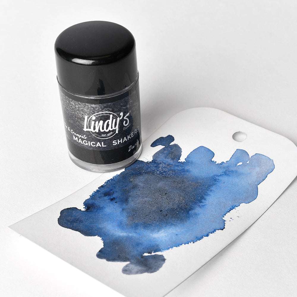 Eine Flasche Lindy's Stamp Gang Magical Shaker mit hochpigmentiertem Pulver steht neben einem Anhänger mit einem leuchtend blauen Tintenklecks, ideal für Papierprojekte.