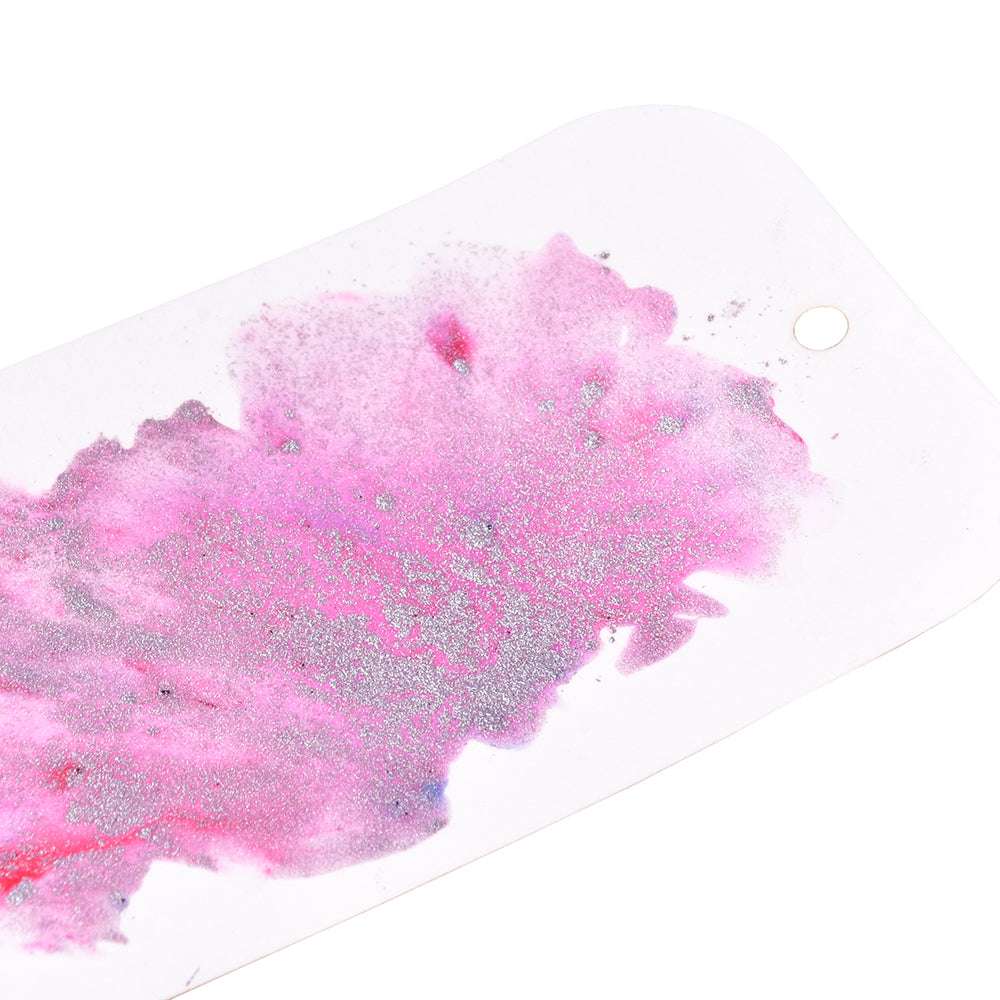 Eine weiße Karte mit rosafarbener und silberner Glitzerfarbe, die mit hochpigmentiertem Pulver von Lindy's Stamp Gang hergestellt wurde, mit einem kleinen Loch in der Ecke.