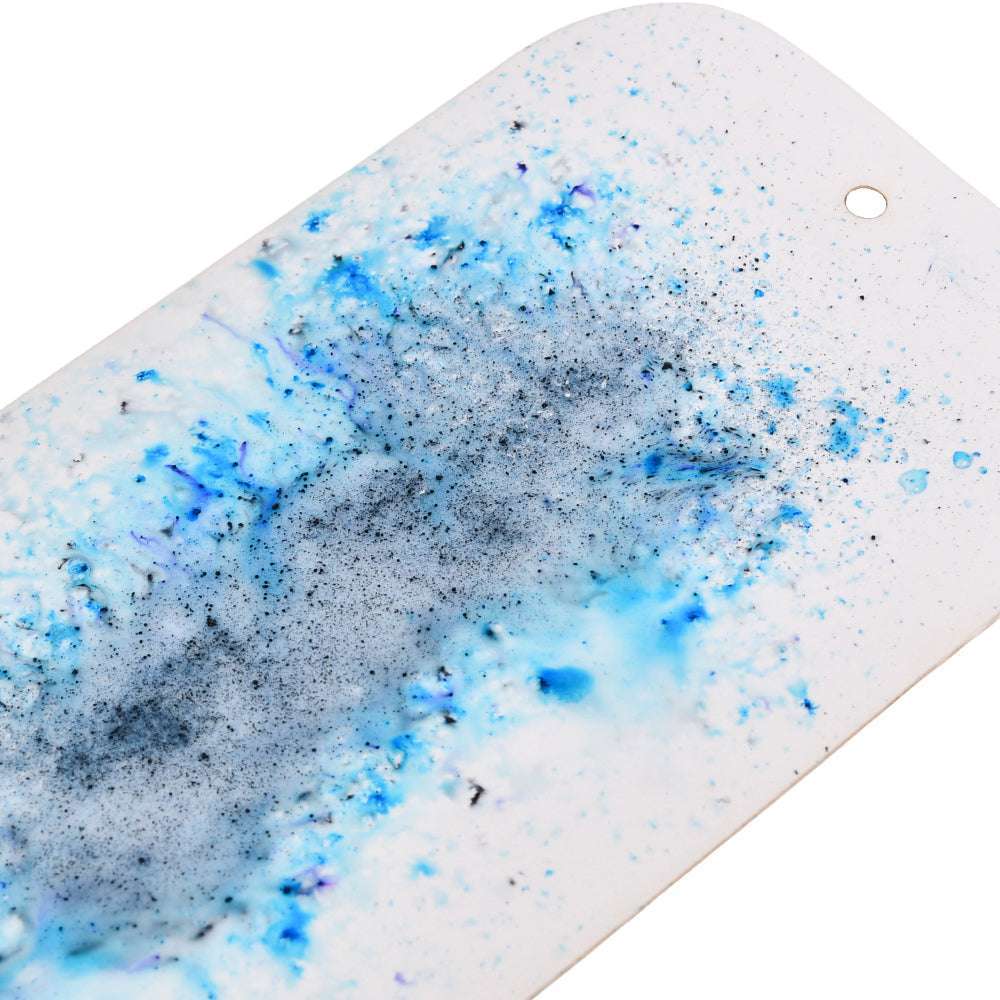 Nahaufnahme eines weißen Lindy's Stamp Gang-Anhängers mit abstrakten blauen und grauen Farbspritzern mit matten Effekten sowie einem kleinen Loch an einem Ende.