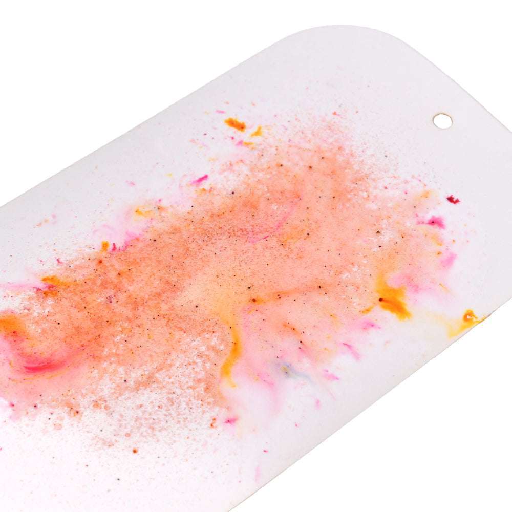 Eine Nahaufnahme von rosafarbenen, orangefarbenen und gelben Lindy's Stamp Gang-Aquarellfarben, die auf weißes Papier gespritzt wurden, mit matten Effekten und leuchtenden Farbmischungen in jedem Spritzer.