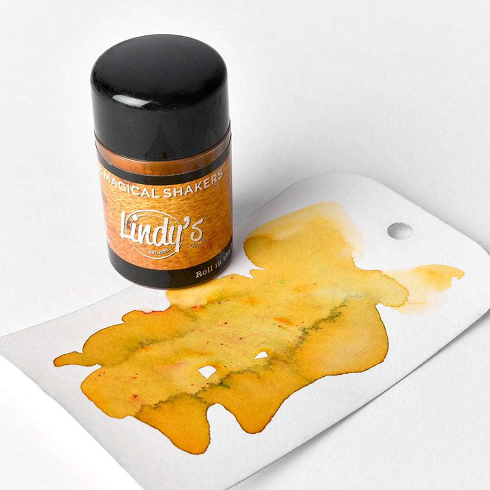 Eine Dose von Lindy's Stamp Gang Magical Shakers mit hochpigmentiertem Pulver, abgebildet mit einem Stück gelber Aquarellfarbe auf einem weißen Anhänger.