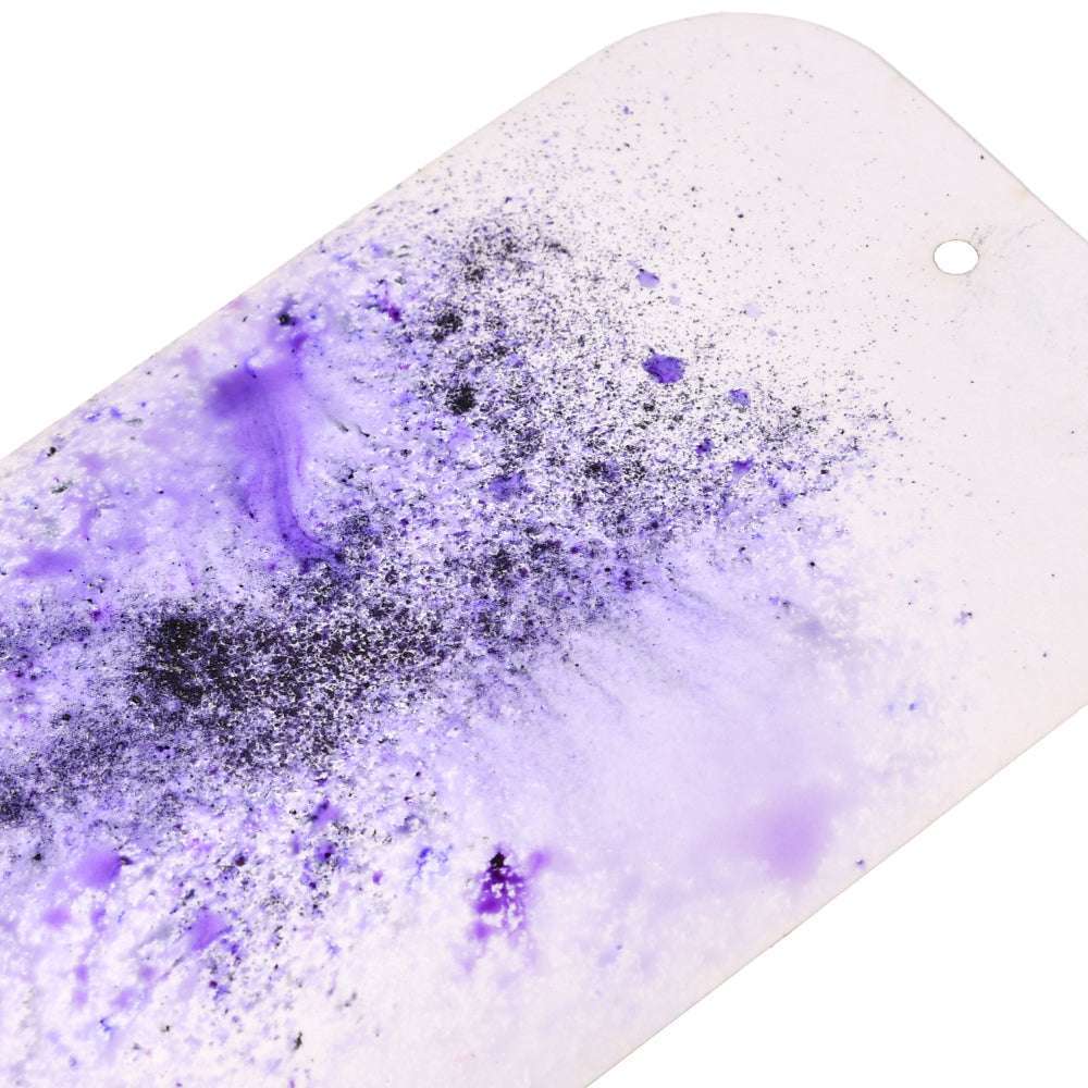 Lila und schwarzes Lindy's Stamp Gang Magical Powder spritzt auf eine weiße, rechteckige Fläche mit kleinem Eckloch und erzeugt auffällige Matteffekte.