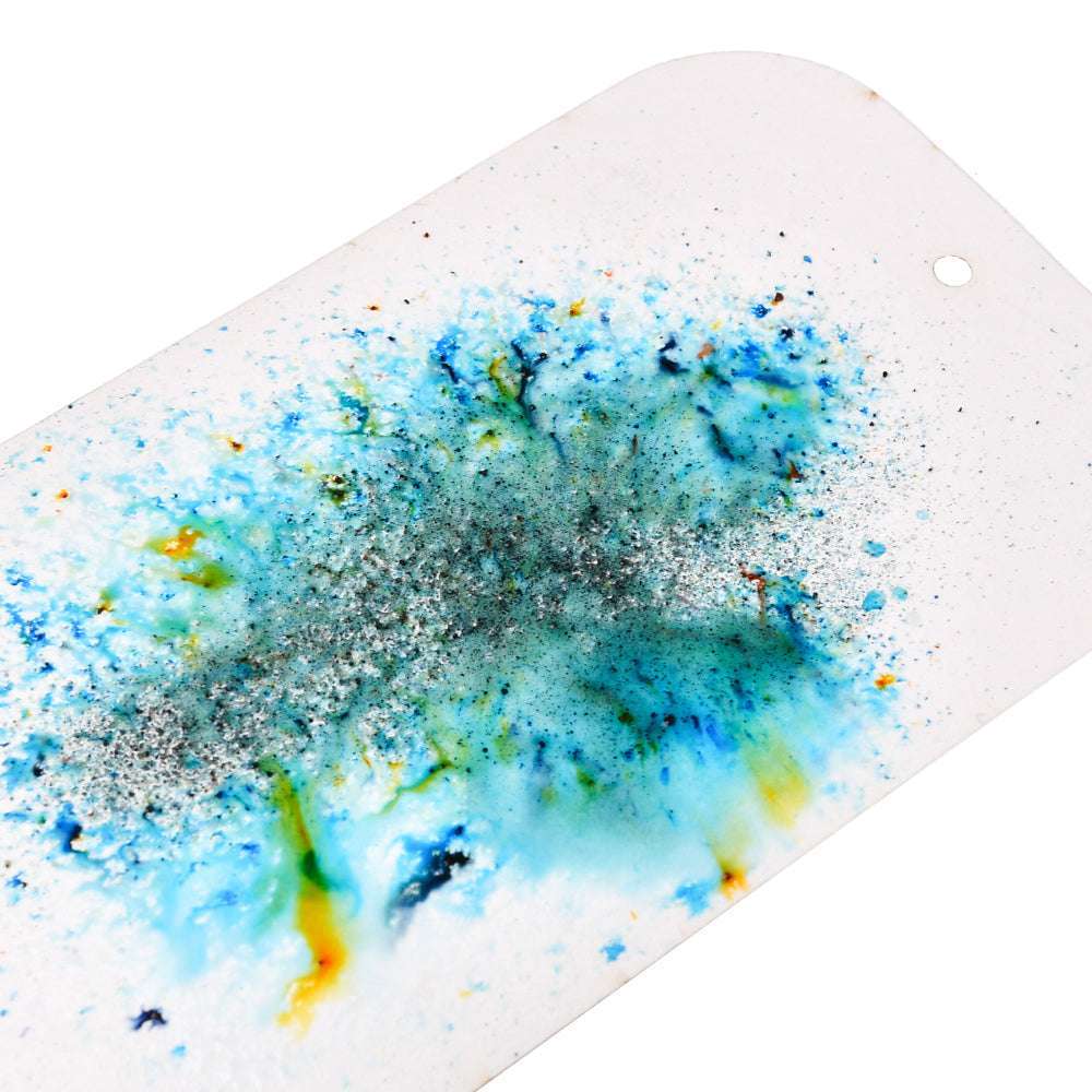 Abstrakte Spritzer aus blauem, grünem, gelbem und silbernem Magical Powder von Lindy's Stamp Gang erzeugen matte Effekte auf einer weißen, rechteckigen Fläche mit abgerundeten Ecken.