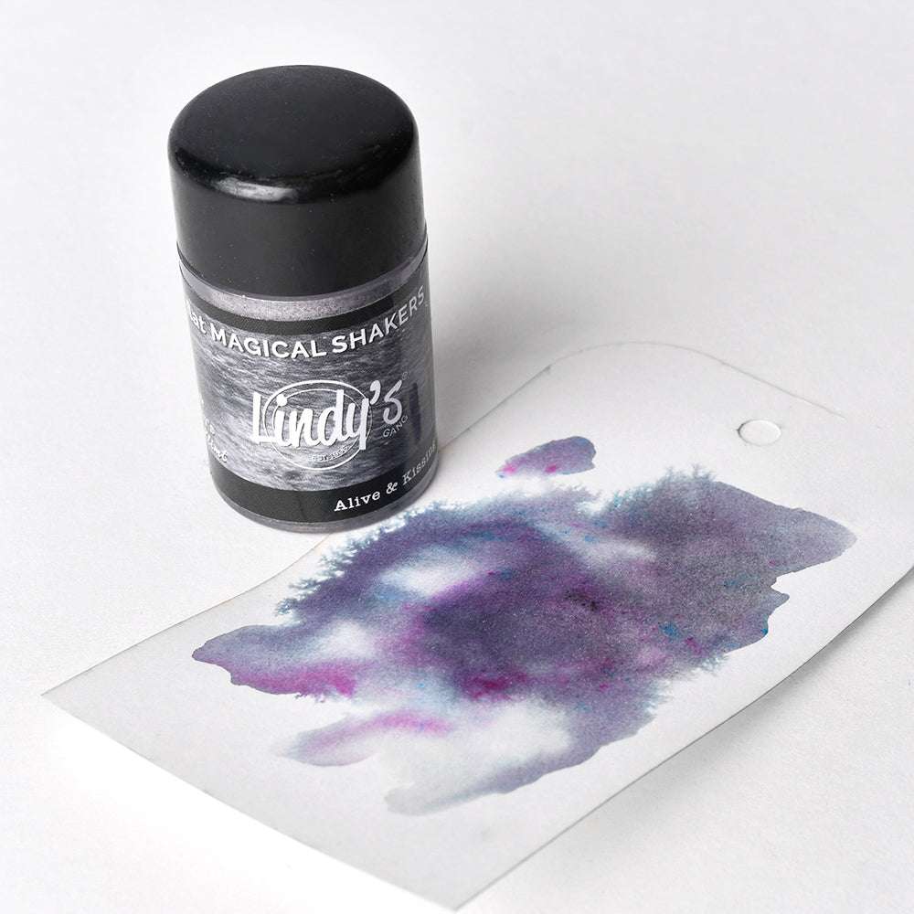 Ein Lindy's Stamp Gang Shaker und ein Anhänger mit violetten und blauen aquarellartigen Flecken auf weißem Papier zeigen die lebendigen Matteffekte dieses hochpigmentierten Pulvers.