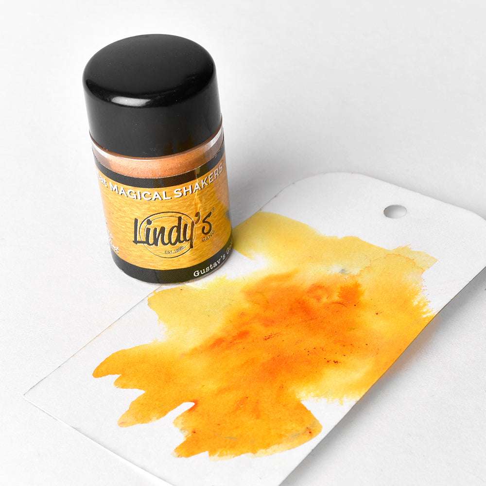 Eine Flasche Lindy's Stamp Gang Magical Shaker Powder steht neben einem Anhänger mit gelb-orangefarbener Aquarellfarbe, die sich perfekt für leuchtende Farbmischungen eignet.