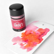 Ein Tiegel mit Lindy's Stamp Gang Puder steht neben einem Anhänger mit kräftigen rosa und orangen Aquarellfarben, die die hochpigmentierte Formel für leuchtende Farbeffekte hervorheben.