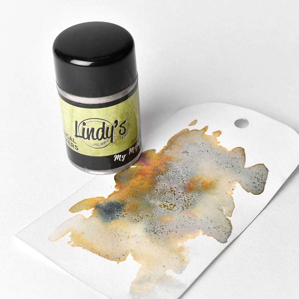 Eine Dose hochpigmentiertes Pulver von Lindy's Stamp Gang steht neben einem weißen Schild mit einem bunten Tintenfleck, der die Brillanz dieses leuchtenden Pulvers hervorhebt.