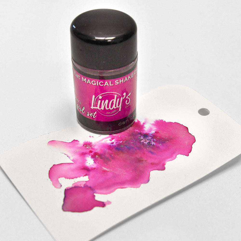 Eine Dose Lindy's Stamp Gang Magical Shaker mit hochpigmentiertem Pulver erzeugt einen rosa und lila Tintenfleck auf einem weißen Anhänger.