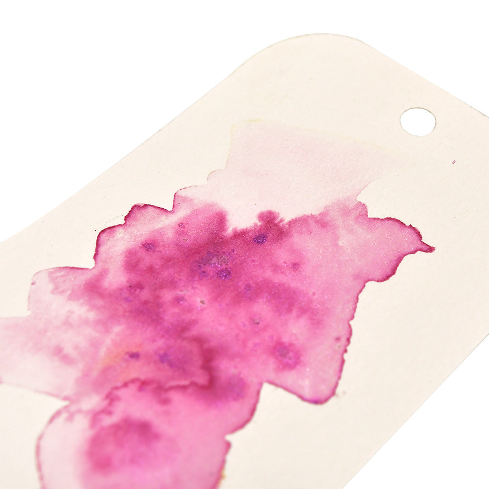 Ein weißer Anhänger von Lindy's Stamp Gang mit einer rosa und violetten Aquarellfarbe, die an Magical Powder Farbmischungen erinnert, und einem Loch an der Spitze.