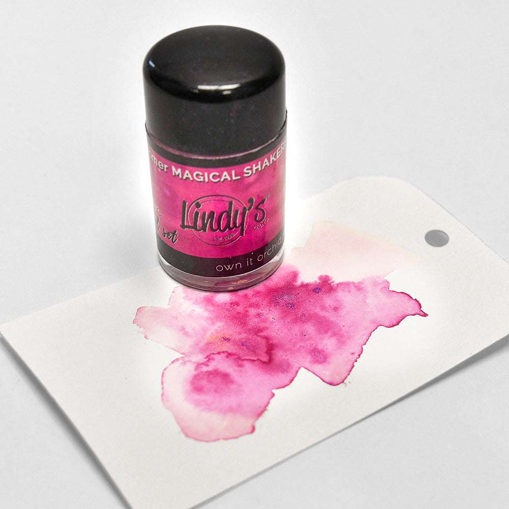 Ein schwarzer Lindy's Stamp Gang Magical Shaker mit hochpigmentiertem Pulver erzeugt einen leuchtend rosa Aquarellfleck auf der Karte.