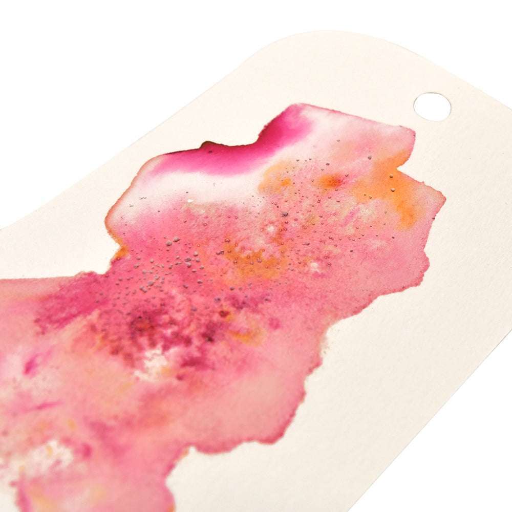 Eine Nahaufnahme eines Aquarells mit Rosa-, Orange- und Gelbtönen auf weißem Papier, das mit Lindy's Stamp Gang hochpigmentiertes Pulver enthält, das sich ideal für lebendige, matte Projekte eignet.