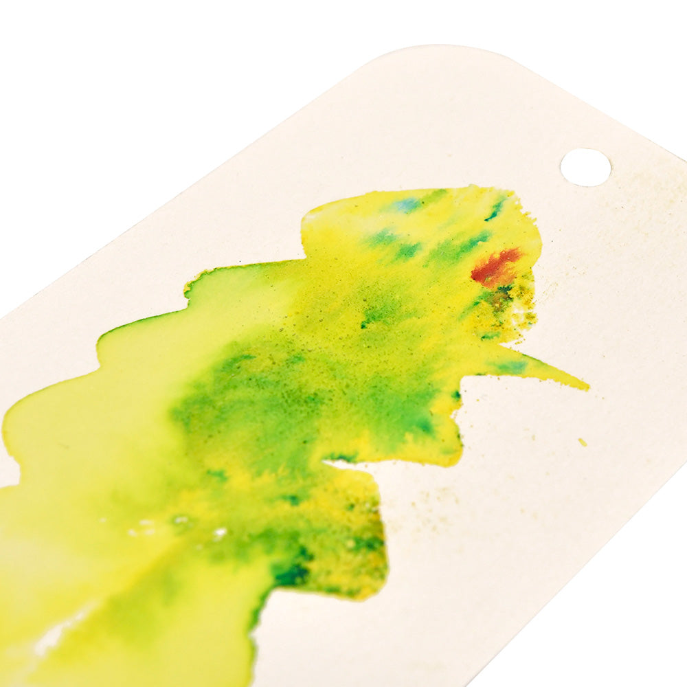 Ein weißer Anhänger mit einem Loch, verziert mit gelber, grüner und einem Hauch roter Wasserfarbe aus den hochpigmentierten Pulvern von Lindy's Stamp Gang.