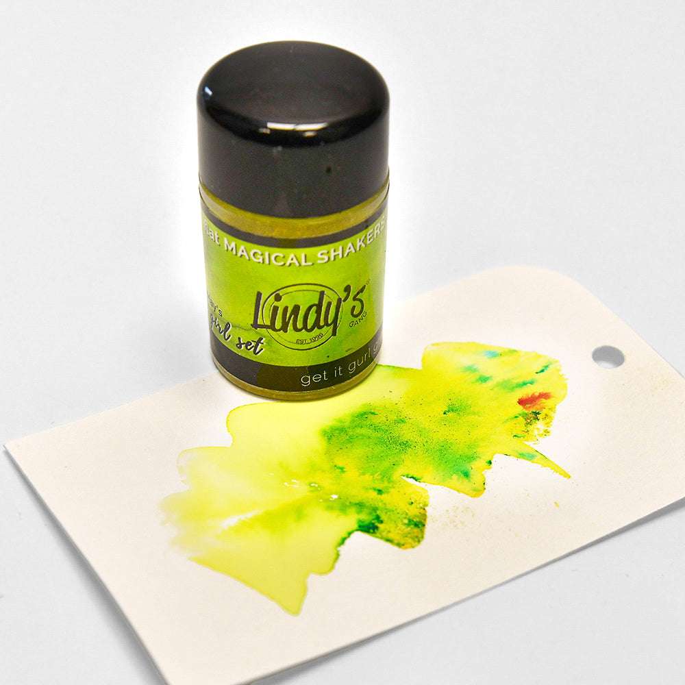 Eine Dose Lindy's Stamp Gang Magical Powder Shaker mit grün-gelbem, einmalig hochpigmentiertem Pulver auf einem weißen Anhänger.