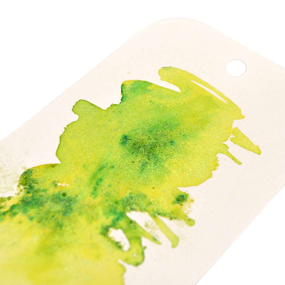 Muster von gelber und grüner Aquarellfarbe von Lindy's Stamp Gang mit hochpigmentiertem Pulver auf weißem Papier mit einer gestanzten Ecke, die einzigartige Farbmischungen hervorhebt.