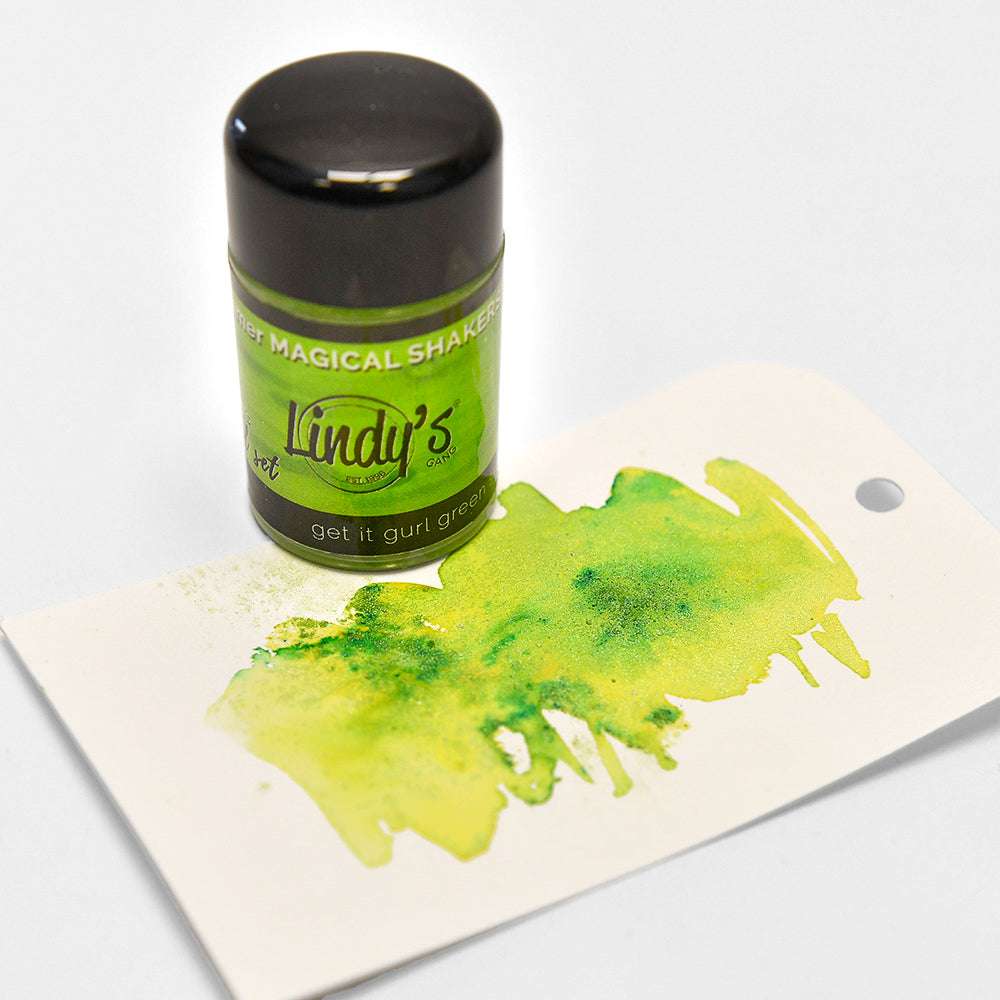 Eine Flasche Lindy's Stamp Gang Magical Powder (hochpigmentiertes Pulver) steht neben einem Anhänger mit einem grünen Aquarellmuster - ideal für kreative Farbmischungen.