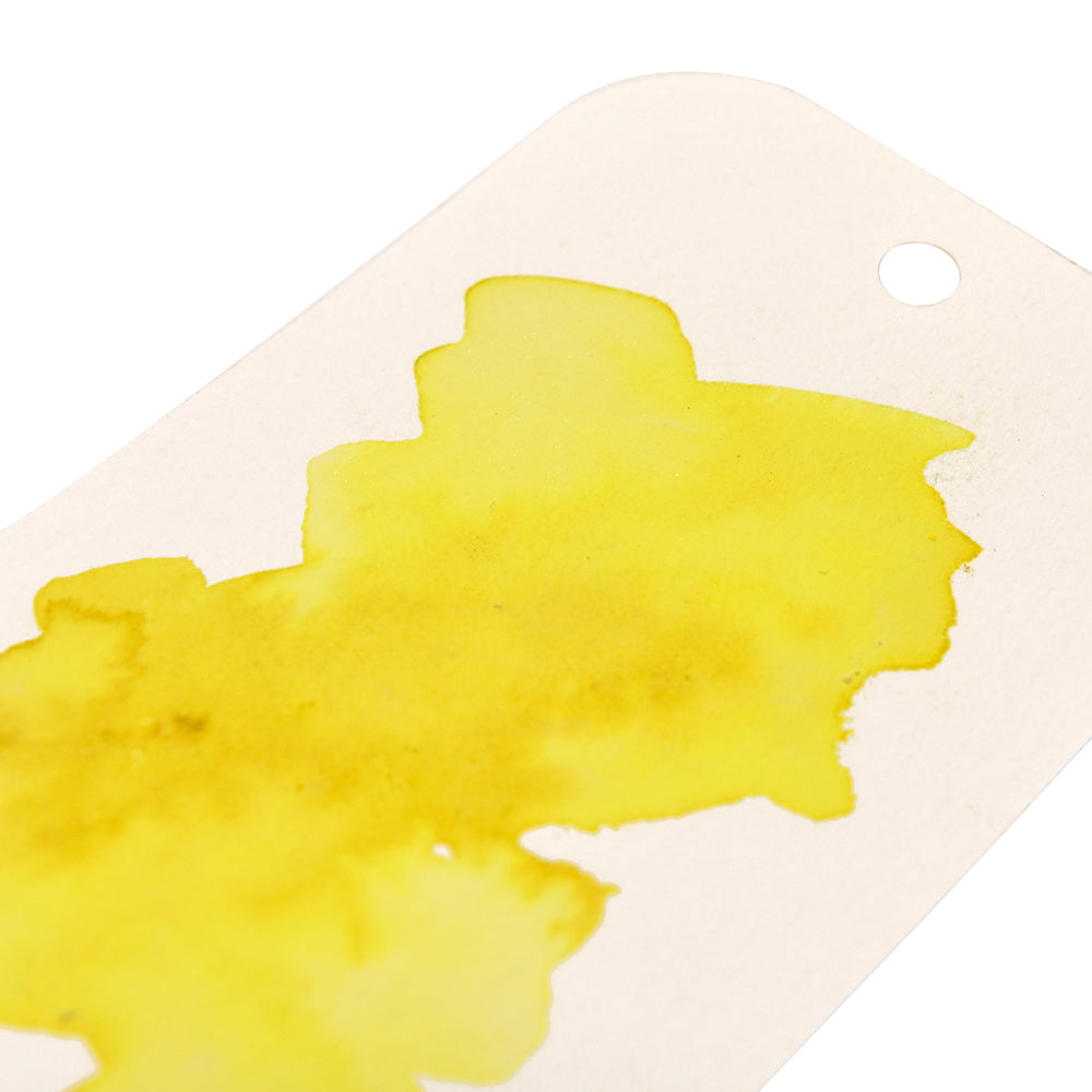 Ein weißer Anhänger mit einem Loch ist mit einem leuchtend gelben Aquarellfleck versehen, der mit Lindy's Stamp Gang hochpigmentiertem Pulver für lebendige Farben und kräftige, matte Farbmischungen auf seiner Oberfläche sorgt.
