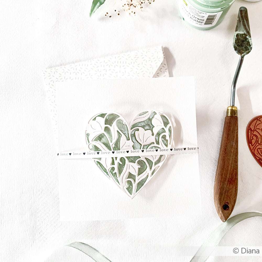 Eine handgefertigte Karte von The Crafters Workshop mit einem Herz aus Blättern und einem "Love"-Streifen auf weißem Grund, hergestellt mit Mixed-Media-Techniken und -Werkzeugen.