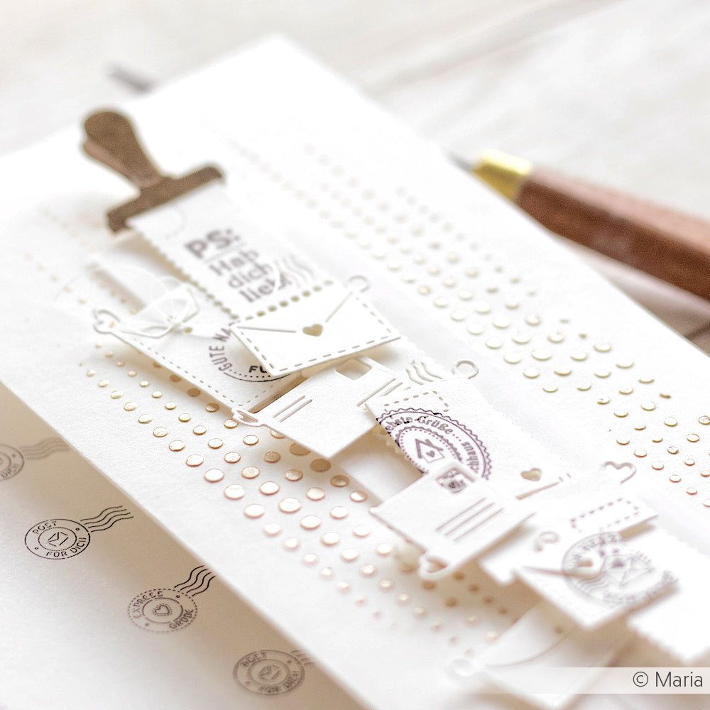 Nahaufnahme einer handgefertigten Karte mit geschichteten Papierumschlägen und gestempelten Postmotiven, akzentuiert mit The Crafters Workshop Mixed Media Techniken und Stencil Butter für dimensionale Textur auf einem strukturierten Hintergrund.