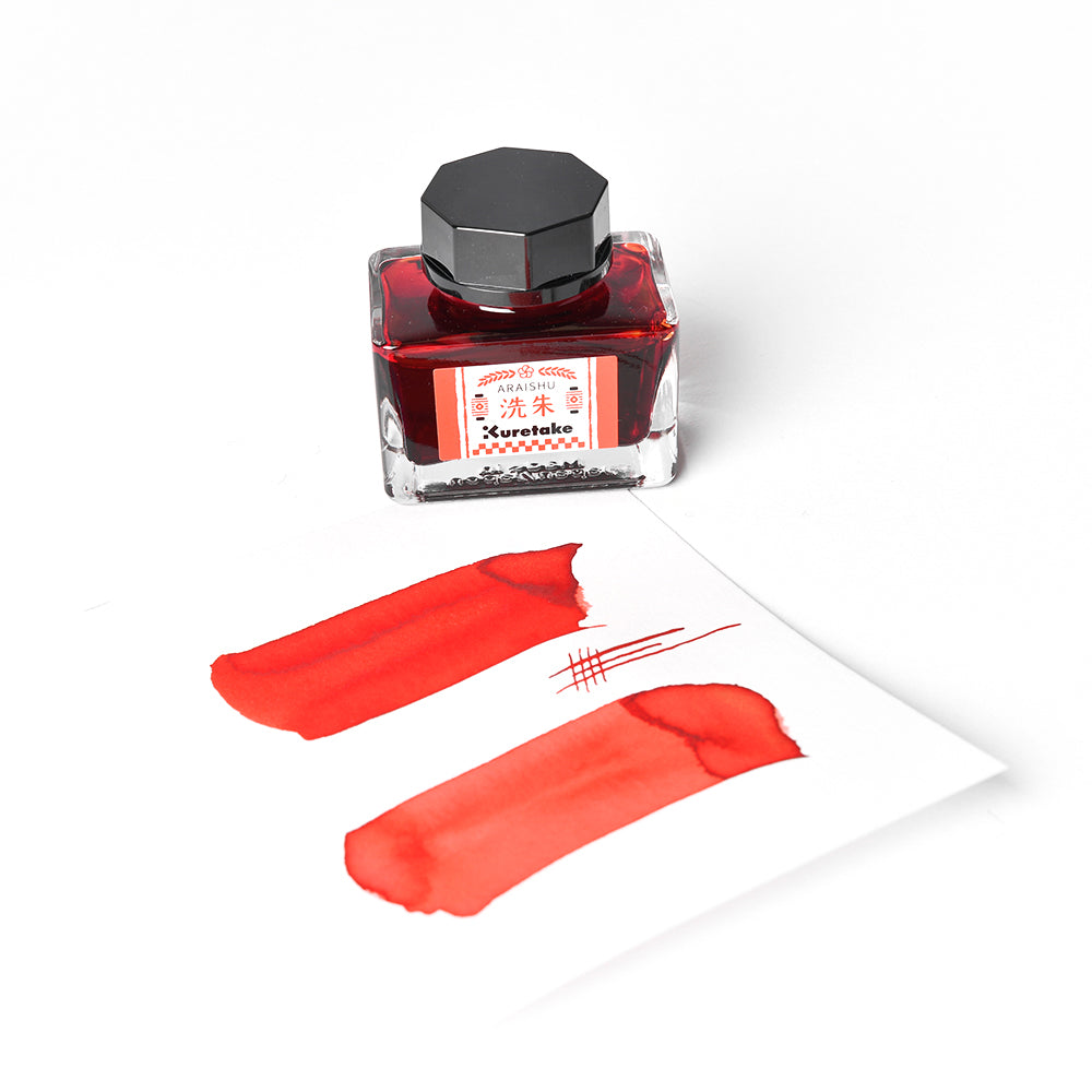 Ein Fläschchen mit roter Farbtinte von Kuretake steht neben einem Papier mit Mustern und Strichen in demselben leuchtenden Farbton, das Teil der vom Japan der Meiji-Ära inspirierten Kollektion MEIJI NO IRO ist.