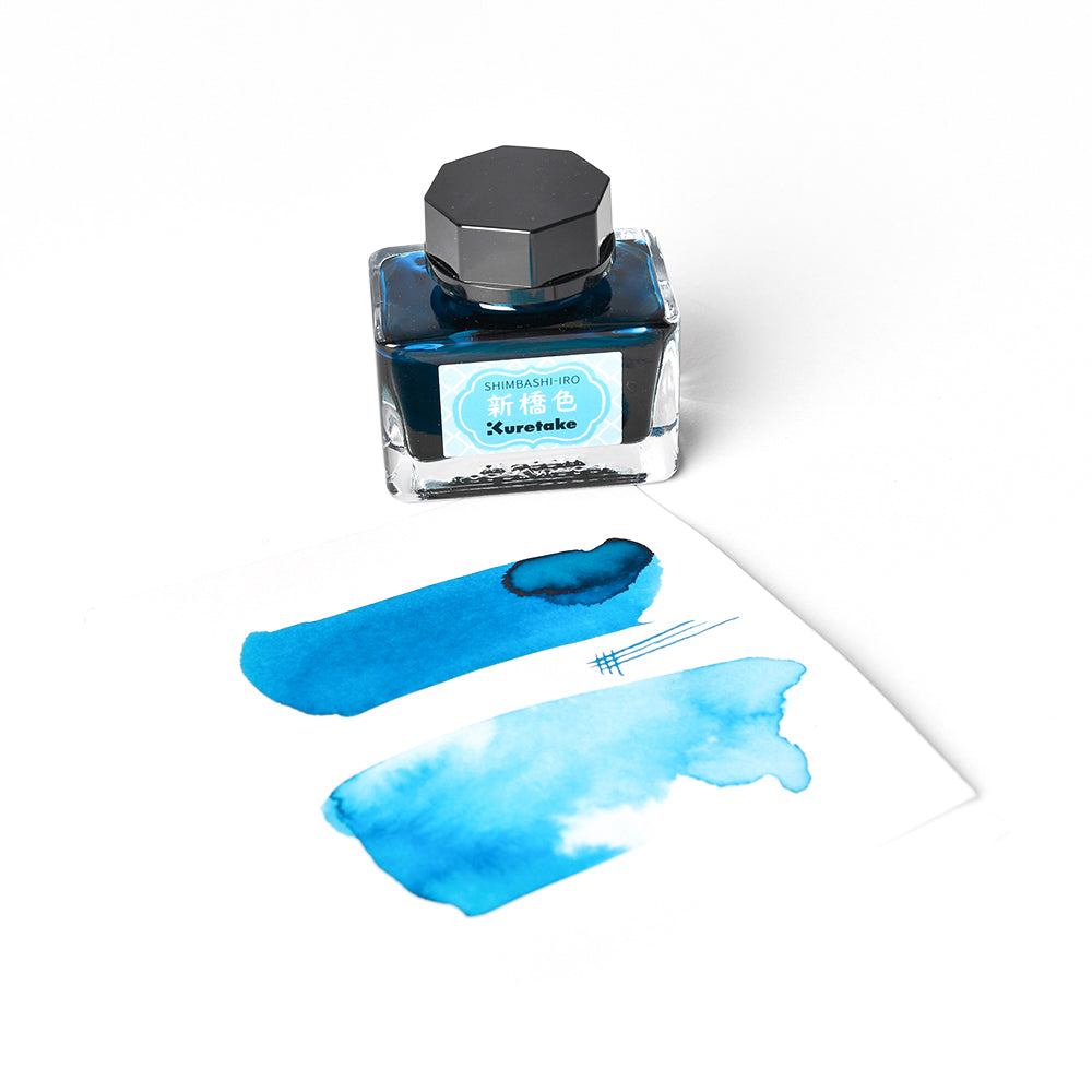 Ein Fläschchen mit blauer Kuretake-Tinte MEIJI NO IRO steht neben einem Papier mit blauen Flecken und Linien, die von der Meiji-Ära inspiriert sind.