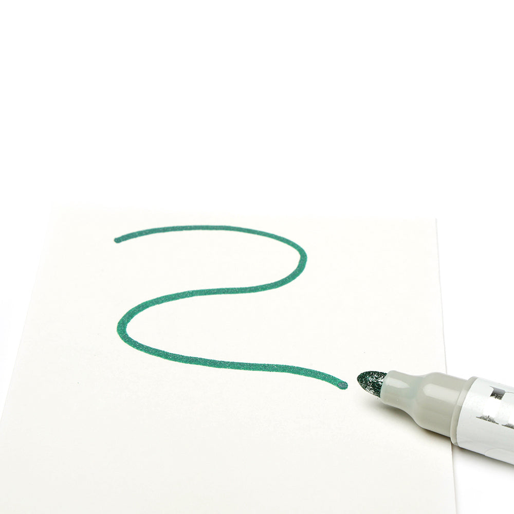 Ein grüner Glittermarker von Tonic Studios zeichnet eine schimmernde, geschwungene Linie auf weißes Papier - ideal für kreative Bastelprojekte.