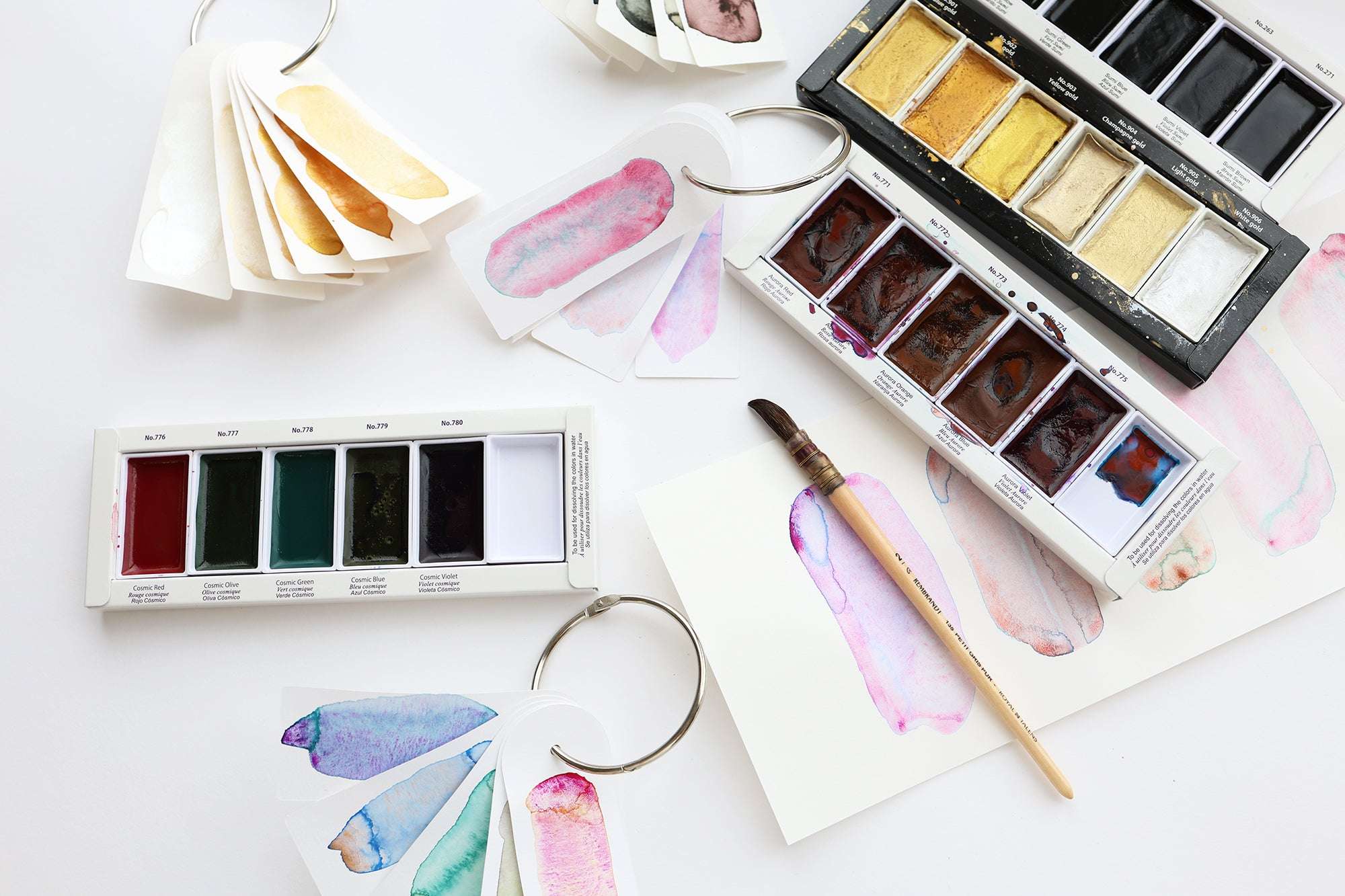 Aquarellpaletten, Farbkleckse auf Ringen und ein Pinsel auf einer weißen Fläche.