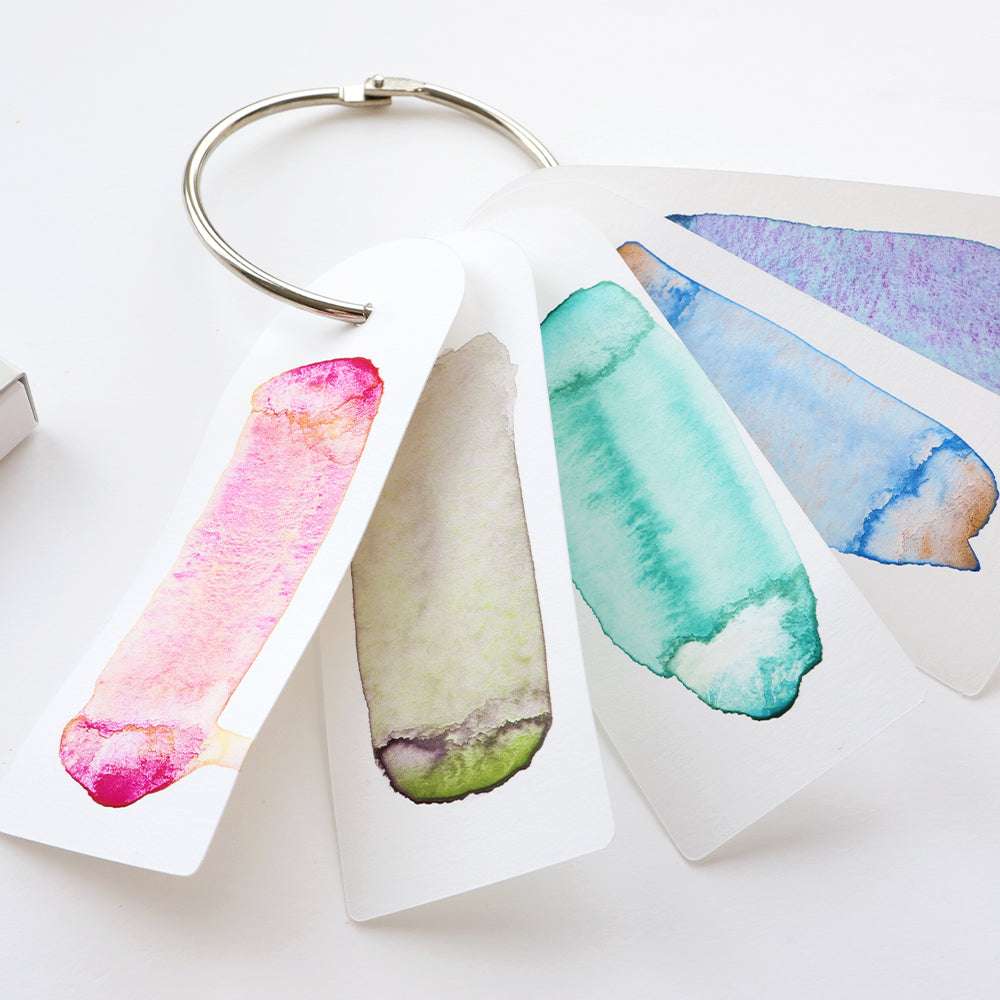 Vier Kuretake Aquarellfarben mit granulierenden Farben sind fächerförmig auf Karten dargestellt, die an einem Metallring befestigt sind.