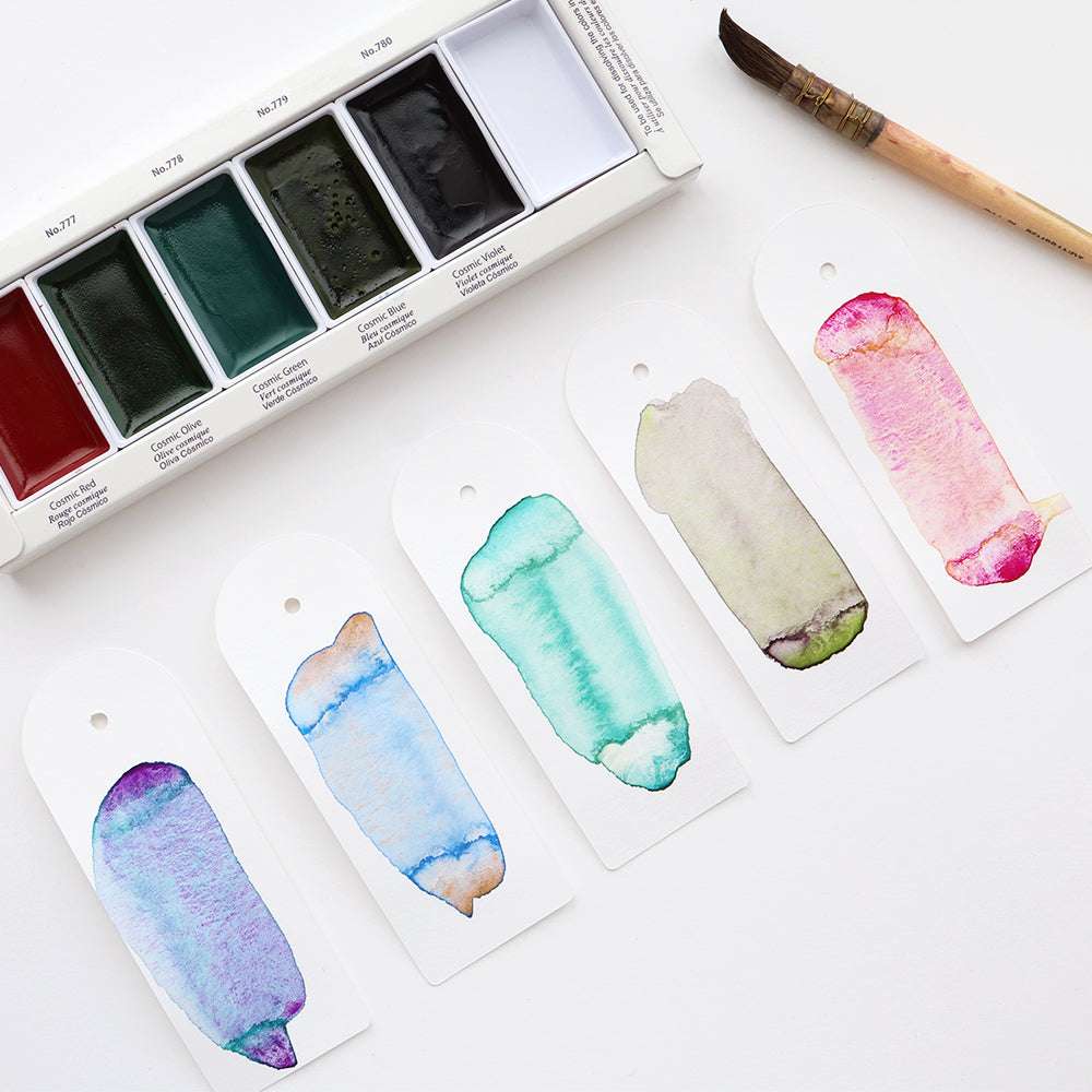 Fünf granulierende Farben sind auf Anhängern neben einem Kuretake Gansai Tambi Aquarellfarbset und einem Pinsel abgebildet, die alle auf einer weißen Fläche ausgestellt sind.