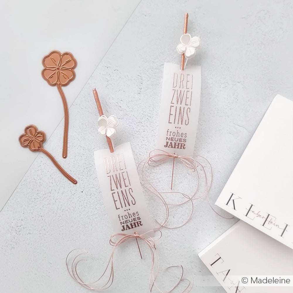 Zwei dekorative Lesezeichen von Alexandra Renke zeigen deutsche Neujahrswünsche, kupferfarbene Blumen und weiße Karten auf hellem Grund, die jeweils elegant mit Makramee-Details gearbeitet sind.