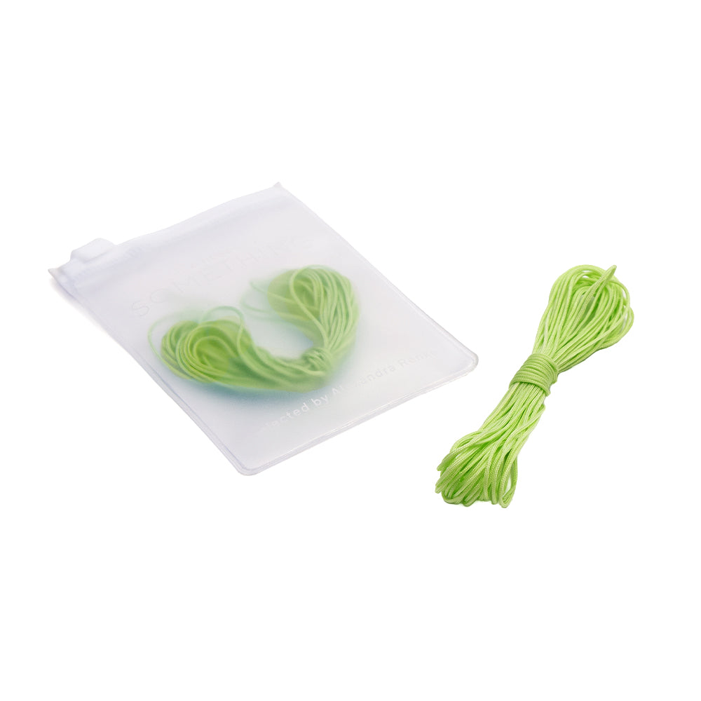 Ein Bündel grüner Gummikordel von Alexandra Renke, ideal für Makramee-Bänder und verschiedene Knotentechniken, liegt neben einem durchsichtigen Reißverschlussbeutel, der weitere grüne Gummikordeln enthält.