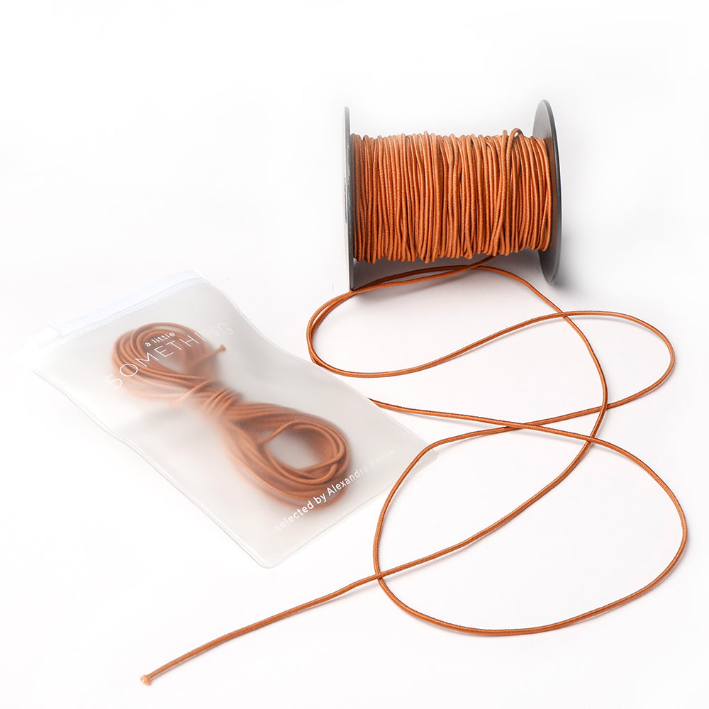 Eine Spule mit brauner Kordel von Alexandra Renke, perfekt für das Bastelprojekt, wird mit losen und gebündelten Kordeln in einem transparenten Beutel geliefert.