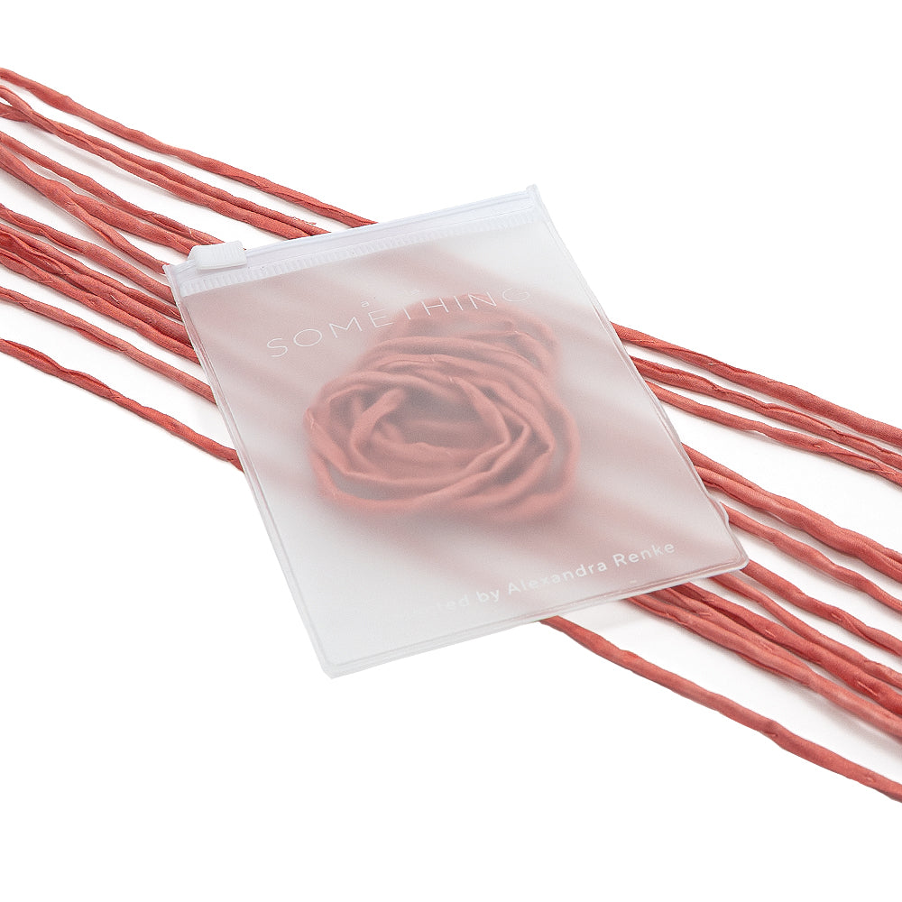 Ein mattes Reißverschluss-Säckchen von ☆ mit einem zarten Rosenmotiv, präsentiert auf rosa Seidenschnur – ideal für die Gestaltung eleganter Geschenkverpackungen.