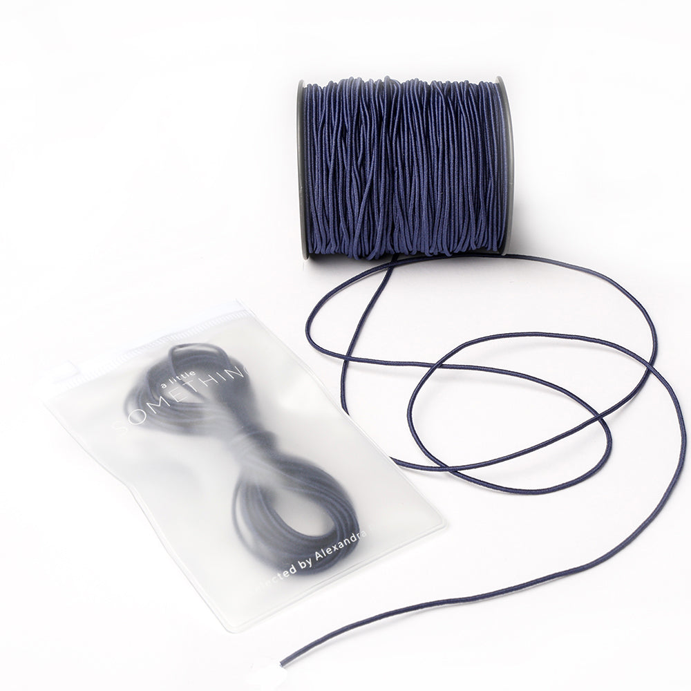 Eine Spule marineblaues Elastikband von Alexandra Renke mit abgewickelter Kordel und zusätzlicher Kordel in einem versiegelten Beutel - ideal für Ihr nächstes Bastelprojekt.