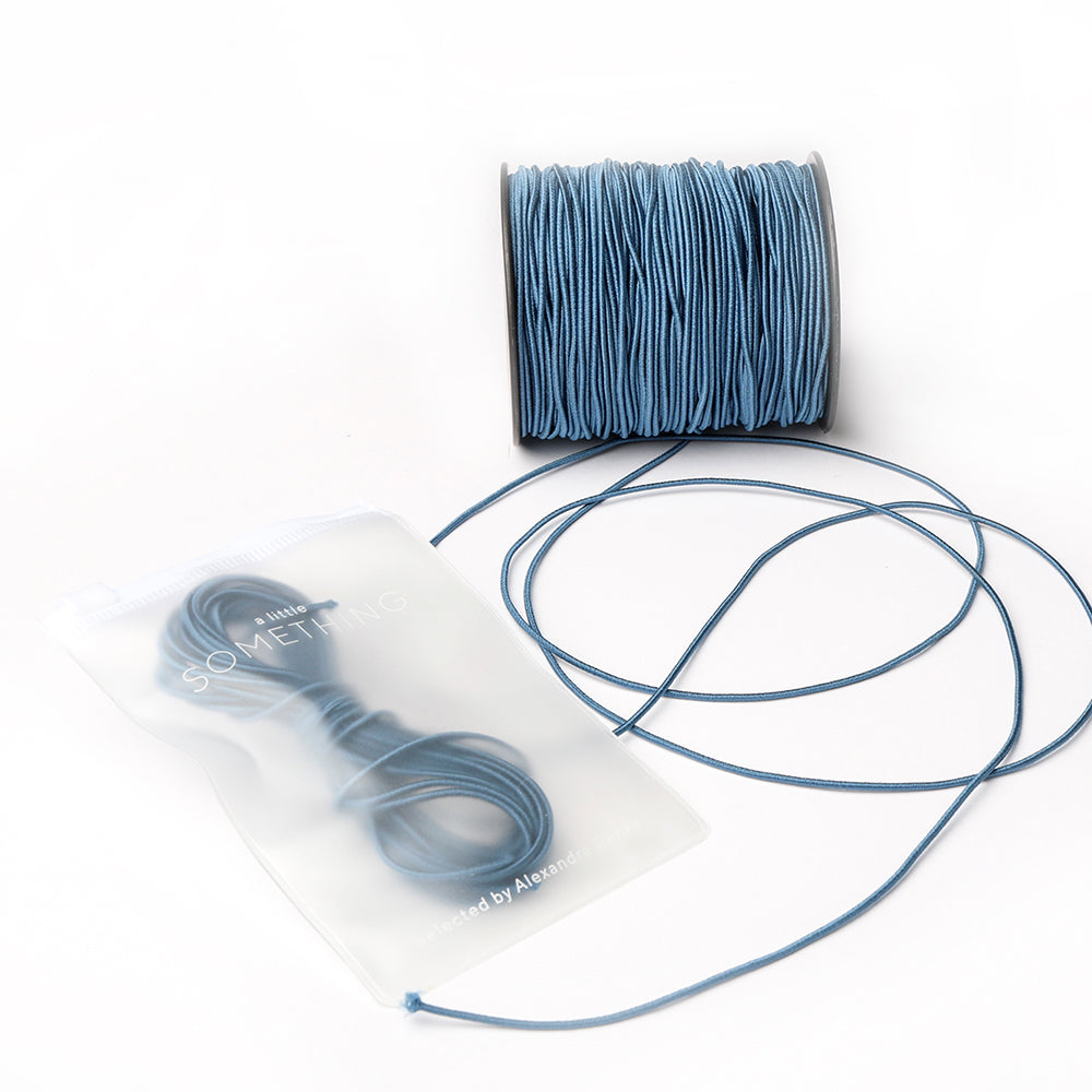 Eine Spule blaues Elastikband von Alexandra Renke mit Schnur in einem durchsichtigen Plastikbeutel - ideal für jedes Bastelprojekt - auf weißem Hintergrund.