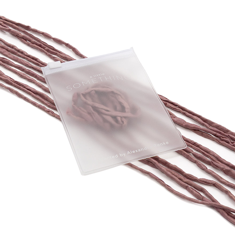 Ein mattierter Beutel von ☆ mit Schriftzug auf mauvefarbenem, handgenähtem Stoff und schimmernder Seidenkordel vor weißem Hintergrund – perfekt für eine elegante Geschenkverpackung.