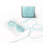 Eine Spule hellblaues Alexandra Renke Elastikband mit einem passenden Bündel in einem durchsichtigen Beutel, perfekt für Ihr nächstes Bastelprojekt, auf weißem Hintergrund.