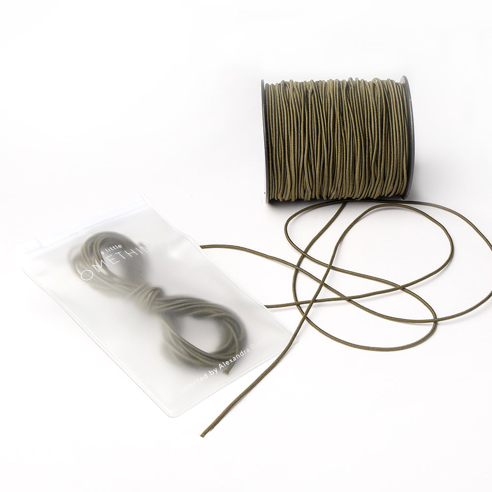 Olivgrünes Elastikband von Alexandra Renke, gewickelt auf einer Spule mit einem kleinen Bündel in einem durchsichtigen, wiederverschließbaren Beutel - ideal für Ihr nächstes Bastelprojekt.