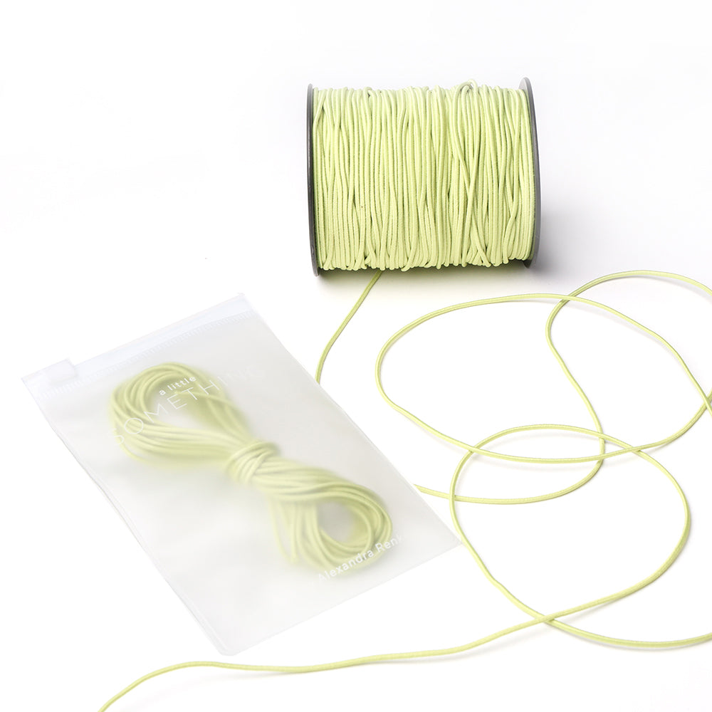 Eine Spule und ein Bündel hellgelbes Elastikband von Alexandra Renke, mit einem Bündel in einem halbtransparenten Beutel - perfekt für Ihr nächstes Bastelprojekt.