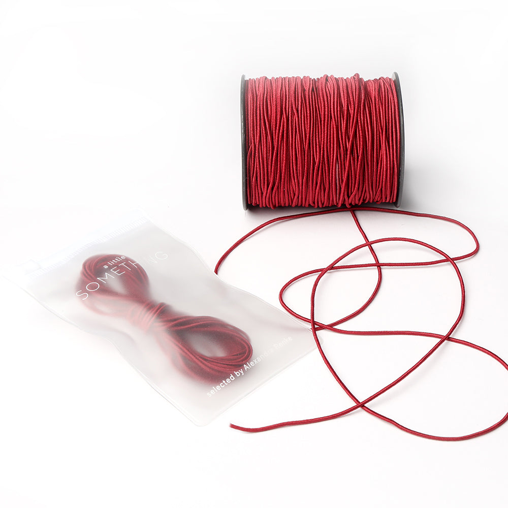 Eine Spule rotes Elastikband von Alexandra Renke mit einem losen Abschnitt und einem kleineren Bündel in einem transparenten Beutel - ideal für jedes Bastelprojekt.