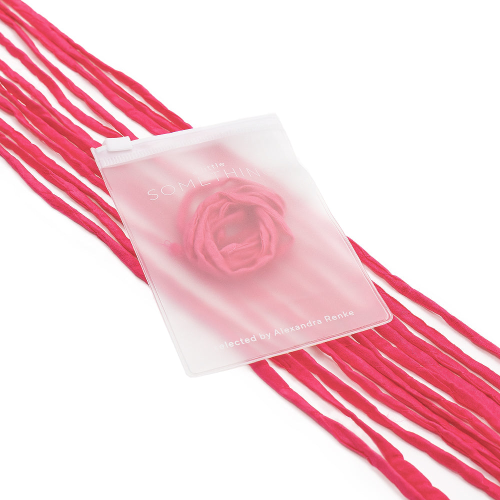 Rosa Seidenschnur-Fäden von ☆ liegen neben einem durchscheinenden, handgenähten Beutel mit Rosenmotiv und Schriftzug auf weißem Hintergrund – ideal für stilvolle Geschenkverpackungen.