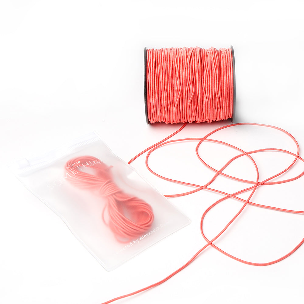 Eine Spule rosa Elastikband von Alexandra Renke mit einem losen Strang neben einem wiederverschließbaren Beutel mit weiterer rosa Kordel - ideal für Ihr nächstes Bastelprojekt.