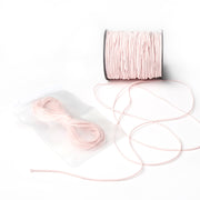 Eine Spule hellrosa Elastikband von Alexandra Renke, mit etwas abgewickelter Kordel und einem versiegelten Beutel mit zusätzlicher rosa Kordel - ideal für jedes Bastelprojekt.