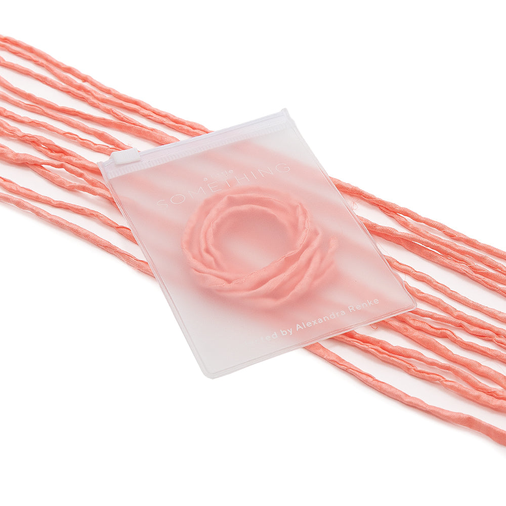 ☆ Rosa, handgefertigte Stoffkordeln mit passender Seidenschnur, stilvoll aufgerollt in einem matten Beutel vor weißem Hintergrund – ideal für elegante Geschenkverpackungen.
