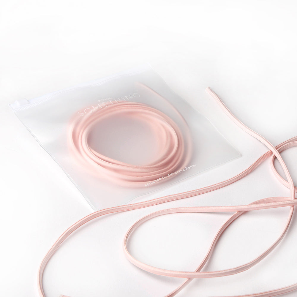 Ein gewundenes rosa Alexandra Renke Elastikband, teilweise in einem gefrosteten Reißverschlussbeutel auf weißem Hintergrund - ideal für Ihr nächstes Bastelprojekt.